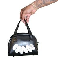 a hand holding a black purse with a smiley face on it